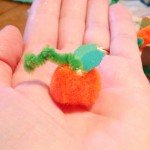 Create your 5 pumpkins by cutting a stem from a green pipe cleaner. Glue stem to top of pom-pom ball. Use leaf shaped punch to punch out leaf from green paper. Glue leaf to pom-pom ball next to stem.